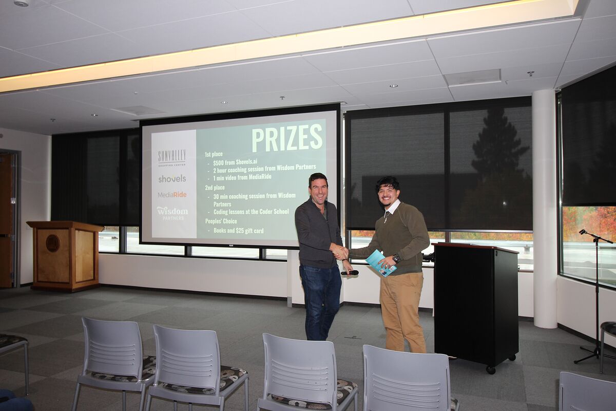 Two people shake hands in front of the projected prizes slide; one holds an award.