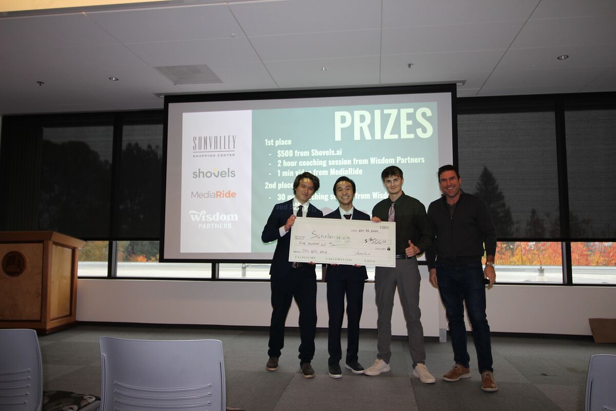 Three members of the Scholarise.org team hold an oversized $500 check with an organizer, standing in front of the prizes slide.
